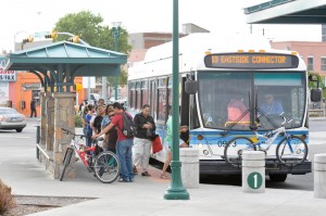 photo of a Sun Metro bus with a bike rack on the front at a bus stop where bicyclists and pedestrians are present